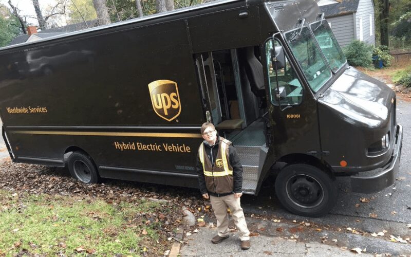 Jake in his new UPS uniform standing in front of delivery truck. 