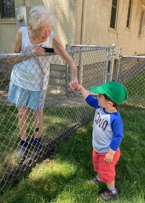 2-year-old Benjamin holding hands with his new friend Mary across their backyard fence. 
